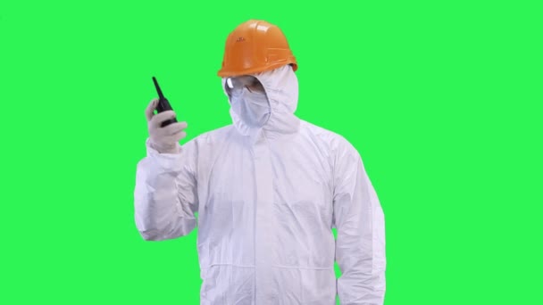 A man in a helmet and protective suit is talking on the walkie-talkie.Green screen background. - Video, Çekim