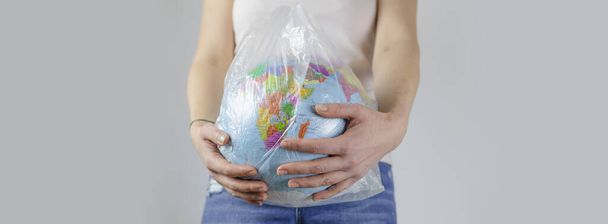 女の子は地球をビニール袋に入れてる。プラスチックフリーコンセプト環境に配慮した廃棄物ゼロのライフスタイル意識的な資源消費。地球生態学。旗 - 写真・画像