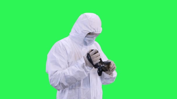 A man in a protective suit and goggles carefully selects the shooting mode in the camcorder.Green screen background. - Metraje, vídeo