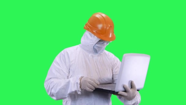 A man in a helmet and protective suit enters data into a computer.Green screen background. - Video, Çekim