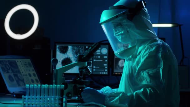 Επιστήμονας με στολή προστασίας και μάσκες που εργάζονται σε ερευνητικό εργαστήριο χρησιμοποιώντας εργαστηριακό εξοπλισμό: μικροσκόπια, δοκιμαστικούς σωλήνες. Coronavirus 2019-ncov κίνδυνος, φαρμακευτική ανακάλυψη, βακτηριολογία και ιολογία - Πλάνα, βίντεο
