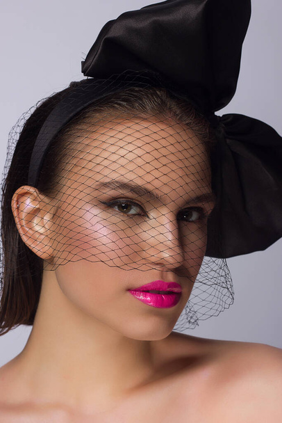 Fashionable half beauty of a woman with a knot and veil, black eyeliner and pink lipstick. Clean and radiant skin, natural lip gloss, thick eyebrows and long eyelashes. Cosmetology and makeup. - Foto, afbeelding