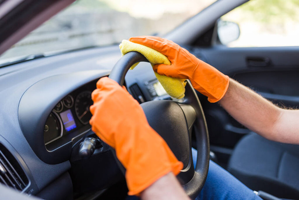 Hands in protective gloves cleaning car steering wheel with microfiber cloth. - Foto, Bild