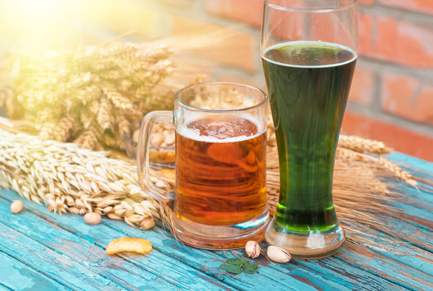 Cerveja verde para o Dia de São Patrício contra o pano de fundo de uma parede de cerâmica fica em uma velha mesa de madeira colorida, juntamente com ingredientes de cerveja - trevo, trigo, cevada e lanches - pistácios, batatas fritas
 - Foto, Imagem