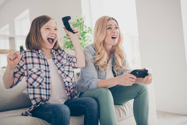 Photo of funny blond lady mom daughter sitting comfy couch joystick play video game winner loser stay home quarantine spend weekend together best friends living room indoors - Foto, imagen
