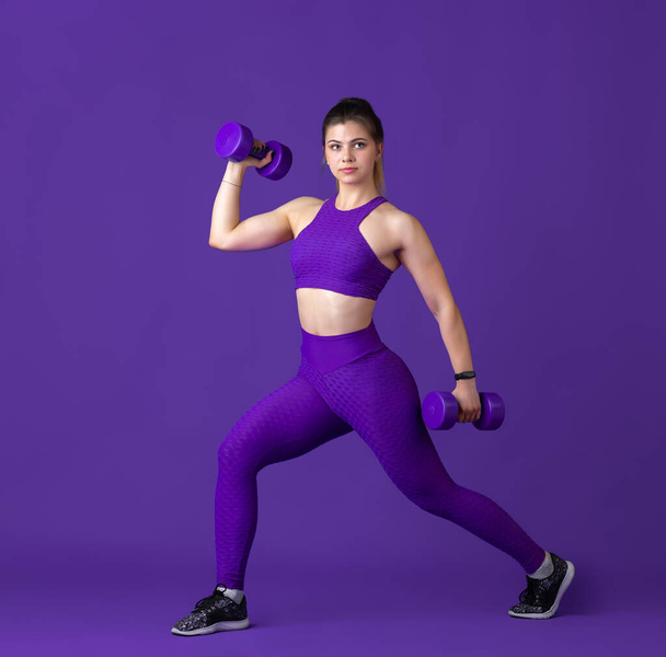 Beautiful young female athlete practicing on purple studio background, monochrome portrait - Foto, Imagem