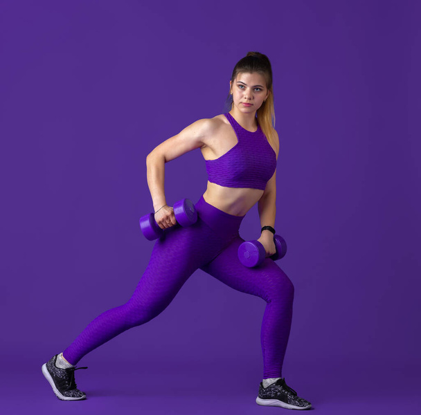 Beautiful young female athlete practicing on purple studio background, monochrome portrait - Fotografie, Obrázek