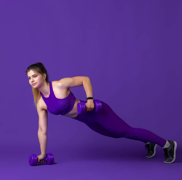 Beautiful young female athlete practicing on purple studio background, monochrome portrait - Fotoğraf, Görsel
