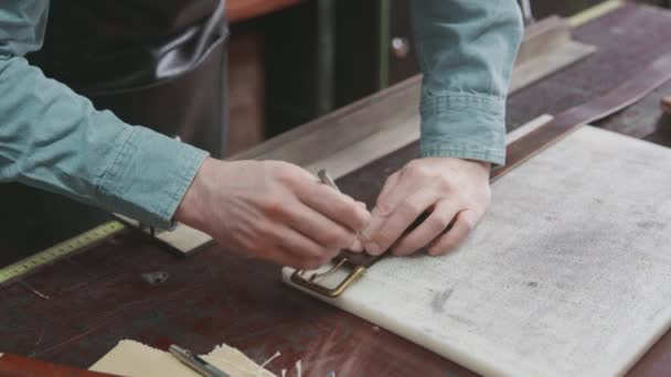 Professioneller Gerber mit Schürze fertigt in der Lederwerkstatt einen neuen braunen Ledergürtel an. Arbeitsprozess des Ledergürtels in der Lederwerkstatt. - Filmmaterial, Video