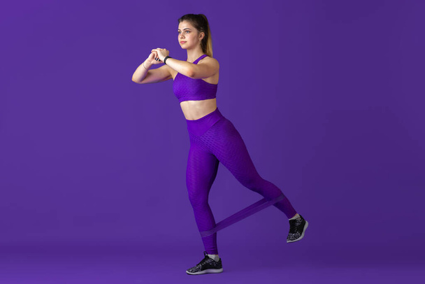 Beautiful young female athlete practicing on purple studio background, monochrome portrait - Foto, imagen