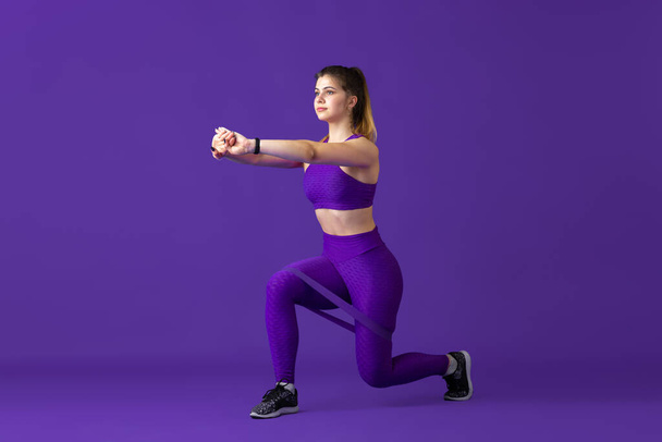 Beautiful young female athlete practicing on purple studio background, monochrome portrait - 写真・画像