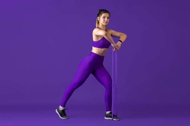 Beautiful young female athlete practicing on purple studio background, monochrome portrait - Zdjęcie, obraz