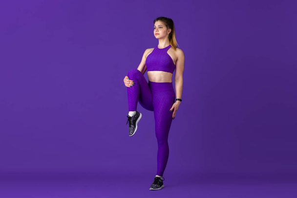 Beautiful young female athlete practicing on purple studio background, monochrome portrait - Valokuva, kuva