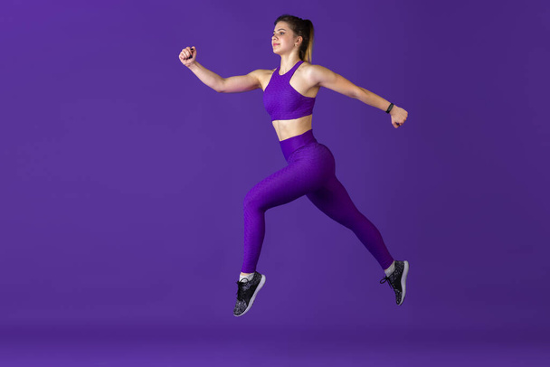 Beautiful young female athlete practicing on purple studio background, monochrome portrait - Фото, изображение