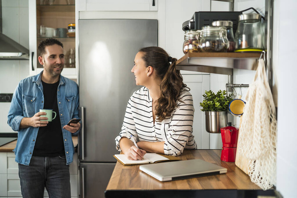 Young Man and Woman Couple talking and making the shopping list in their kitchen at home. Working at home and staying at home. - Foto, Imagen