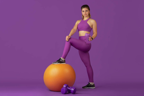 Beautiful young female athlete practicing on purple studio background, monochrome portrait - Photo, Image