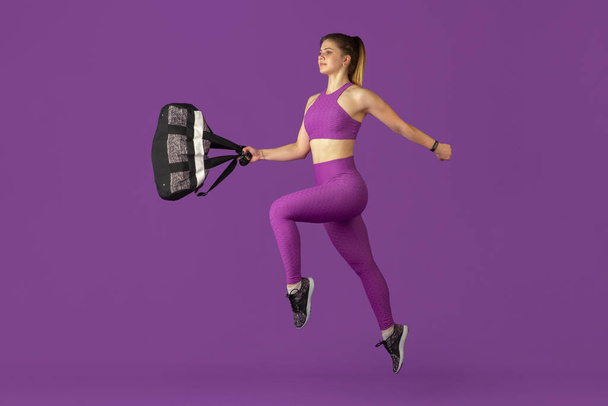 Beautiful young female athlete practicing on purple studio background, monochrome portrait - Фото, изображение