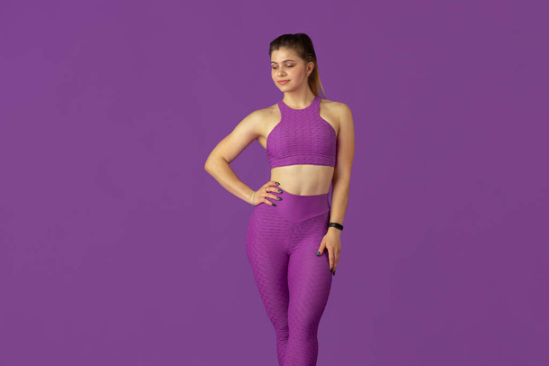 Beautiful young female athlete practicing on purple studio background, monochrome portrait - Fotó, kép