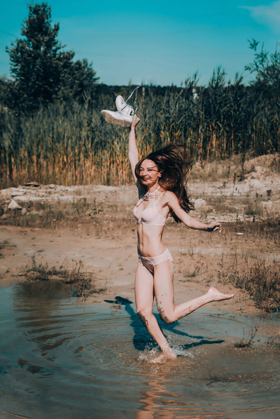 літні канікули. Щаслива усміхнена дівчина в бежевій білизні, розмазана в болоті, що йде, стрибає у воду. позитивні вібрації
. - Фото, зображення