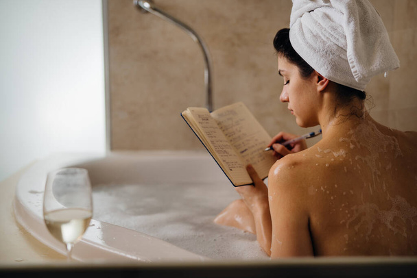 Calm woman having a relaxing bath at home.Spa self care night.Inspired creative person writing gratitude diary/journal.Resolution list.Making plans.Writing thoughts and ideas.Motivation.Enjoying life - Фото, зображення