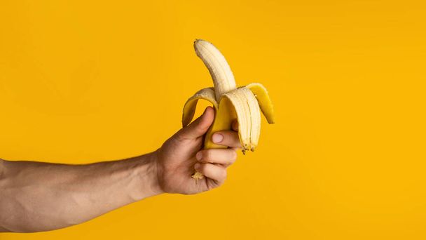 Primo piano di ragazzo che tiene mezza banana sbucciata su sfondo arancione, spazio vuoto. Panorama
 - Foto, immagini
