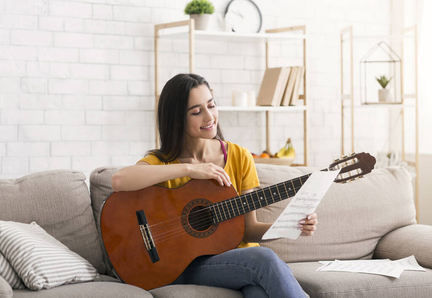 Захоплюючі заходи блокування. Красива дівчина з музичними нотами грає на акустичній гітарі вдома
 - Фото, зображення