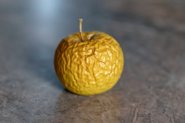 Faltiger gelber alter Apfel liegt auf der Tischplatte, Nahaufnahme auf neutralem Hintergrund. - Foto, Bild