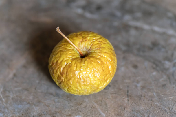 Ζαρωμένο κίτρινο παλιό μήλο βρίσκεται στην κορυφή του τραπεζιού, closeup σε ουδέτερο φόντο. - Φωτογραφία, εικόνα