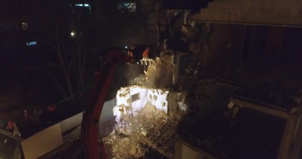 現代の掘削機ブルドーザーと大きなカッターでシャベルは、夜のアパートの建物に囲まれた住宅地の真ん中の建物のファサードを破壊します。. - 映像、動画