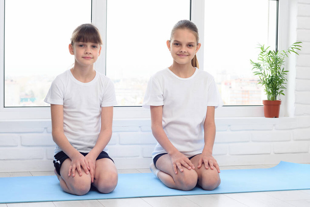 Two sisters are sitting at home on a sports mat before training - Photo, Image