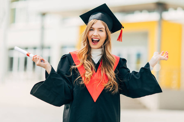 Happy excited beautiful graduate student with a University degree, shows a victory gesture and is happy. Concept of the graduation ceremony - Zdjęcie, obraz