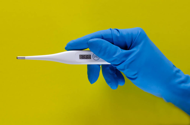 Egy kéz egy kék orvosi kesztyűben 36,2-es hőmérsékletű elektronikus hőmérőt tart. A koncepció a koronavírus, covid-19 tünetei a betegség. - Fotó, kép
