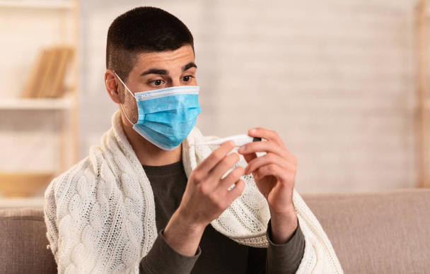 Homem assustado com febre a olhar para o termómetro
 - Foto, Imagem