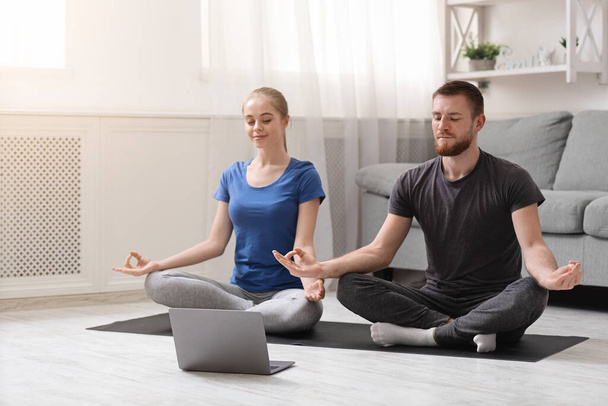 Genç sporcu çift evde eğitmenle meditasyon yapıyor. - Fotoğraf, Görsel