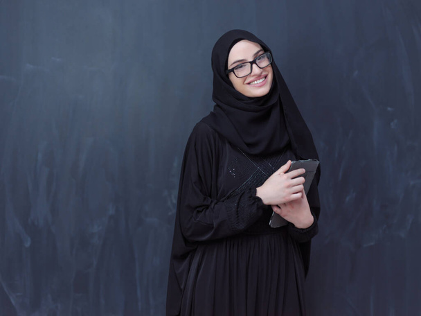 young modern muslim business woman using tablet computer wearing glasses and hijab clothes in front of black chalkboard - Photo, image