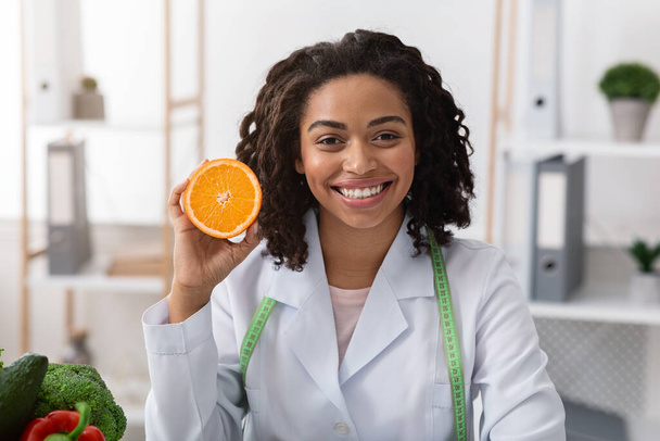 Portret uśmiechniętej lekarki trzymającej pomarańczową połowę - Zdjęcie, obraz