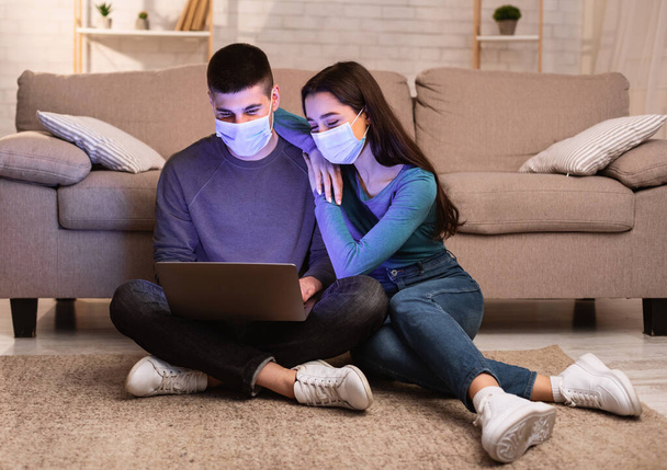 Couple in face masks using laptop sitting on floor - Photo, Image