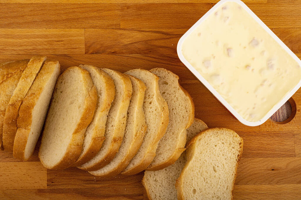 Krájený bochník pšeničného chleba a roztaveného sýra v plastovém tácu na dřevěné řezací desce. Zavřít - Fotografie, Obrázek