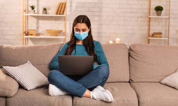 Woman wearing surgical mask using his laptop - Foto, afbeelding