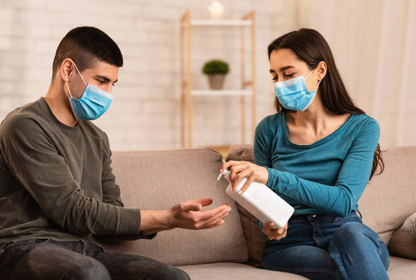 Couple sitting on couch applying anti bacteria spray - Foto, Imagen
