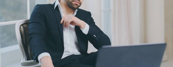 Ritratto panoramico di uomo d'affari in giacca e cravatta seduto sulla sedia di lusso e guardando nel computer portatile
. - Foto, immagini