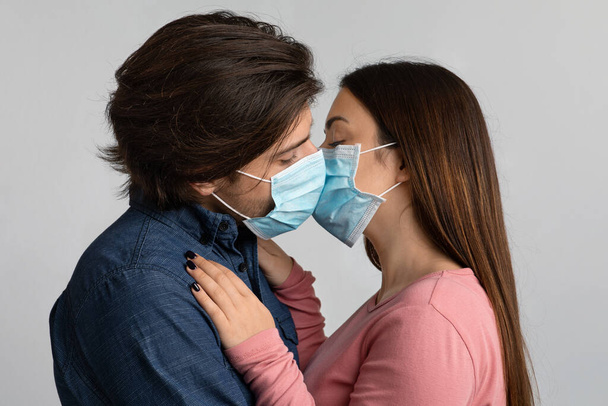Millennial paar kussen elkaar tijdens het dragen van medische gezichtsmaskers - Foto, afbeelding