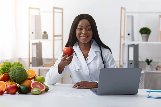 Mooie glimlachende zwarte dokter adviseert het eten van vers fruit - Foto, afbeelding