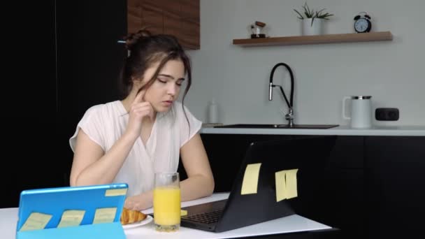 Jonge vrouw in de keuken tijdens quarantaine. Ongelukkig meisje dat thuis werkt. Met laptop en tablet. Bedek gezicht met handen vanwege huilen. - Video