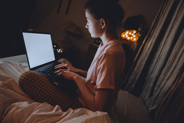 Young woman uses laptop at home in the evening - Фото, изображение