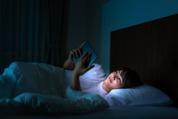 Asiática mulher viciada em celular usando tablet digital navegando na internet para assistir filme ou reunião virtual chamada de vídeo on-line com namorado na cama antes de dormir à noite
 - Foto, Imagem