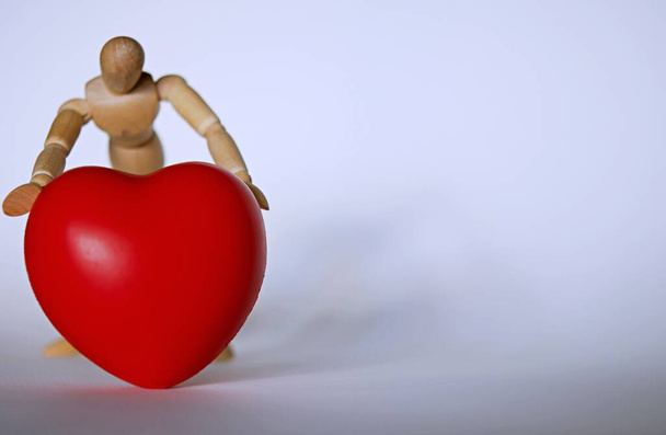 Liefdesbekentenis met houten pop met een rood hart in zijn handen, Valentijnsdag concept. Begrip "bescherming van de gezondheid tegen hartziekten". - Foto, afbeelding
