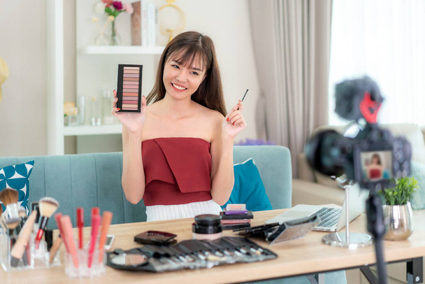 Femme asiatique vlogger présent ou enseigner maquillage produit cosmétique sur son visage et diffuser des vidéos en direct sur le réseau social par Internet à la maison, concept de blogueur beauté
. - Photo, image