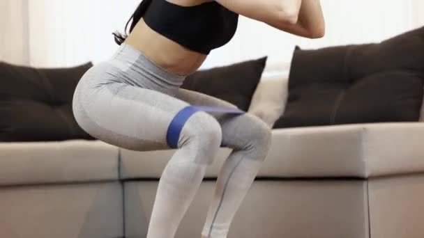 Young woman has workout at home during quarantine. Quick motion. Woman doing squat exercises with sportive gum. Active training in apartment. Low view. - Felvétel, videó