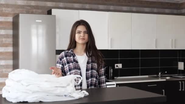 Молодая женщина на кухне во время карантина. Ответственная девушка отталкивает белые пластиковые пакеты и надевает эко-мешок для покупок на столе. Довольная женщина обнимает кошелек
. - Кадры, видео